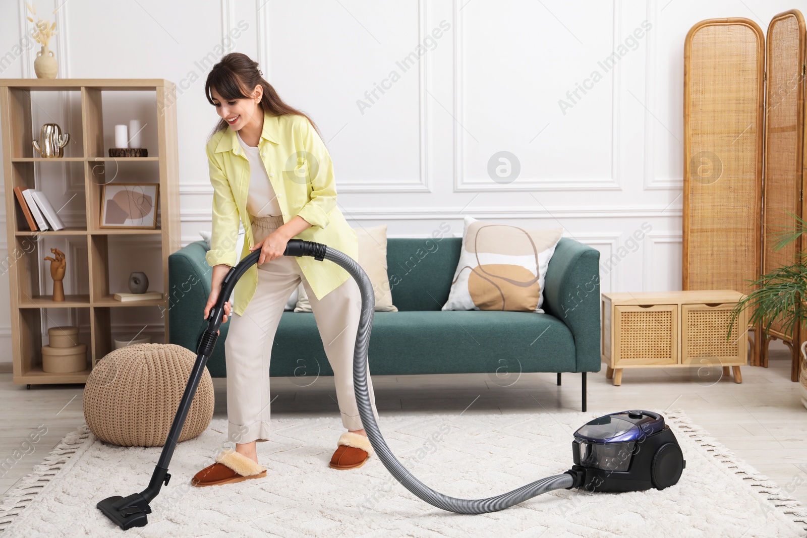 Photo of Young woman vacuuming carpet in living room