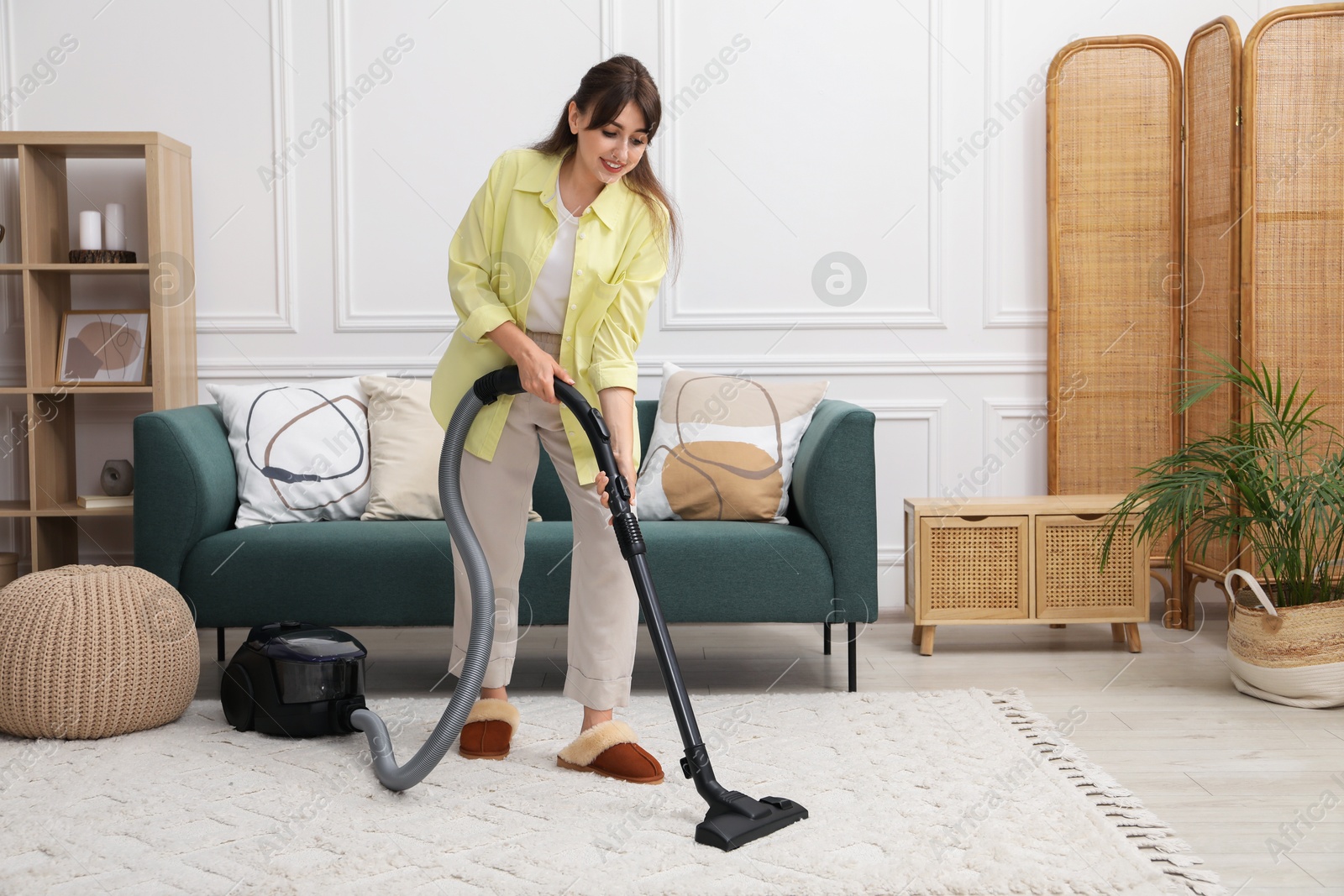 Photo of Young woman vacuuming carpet in living room