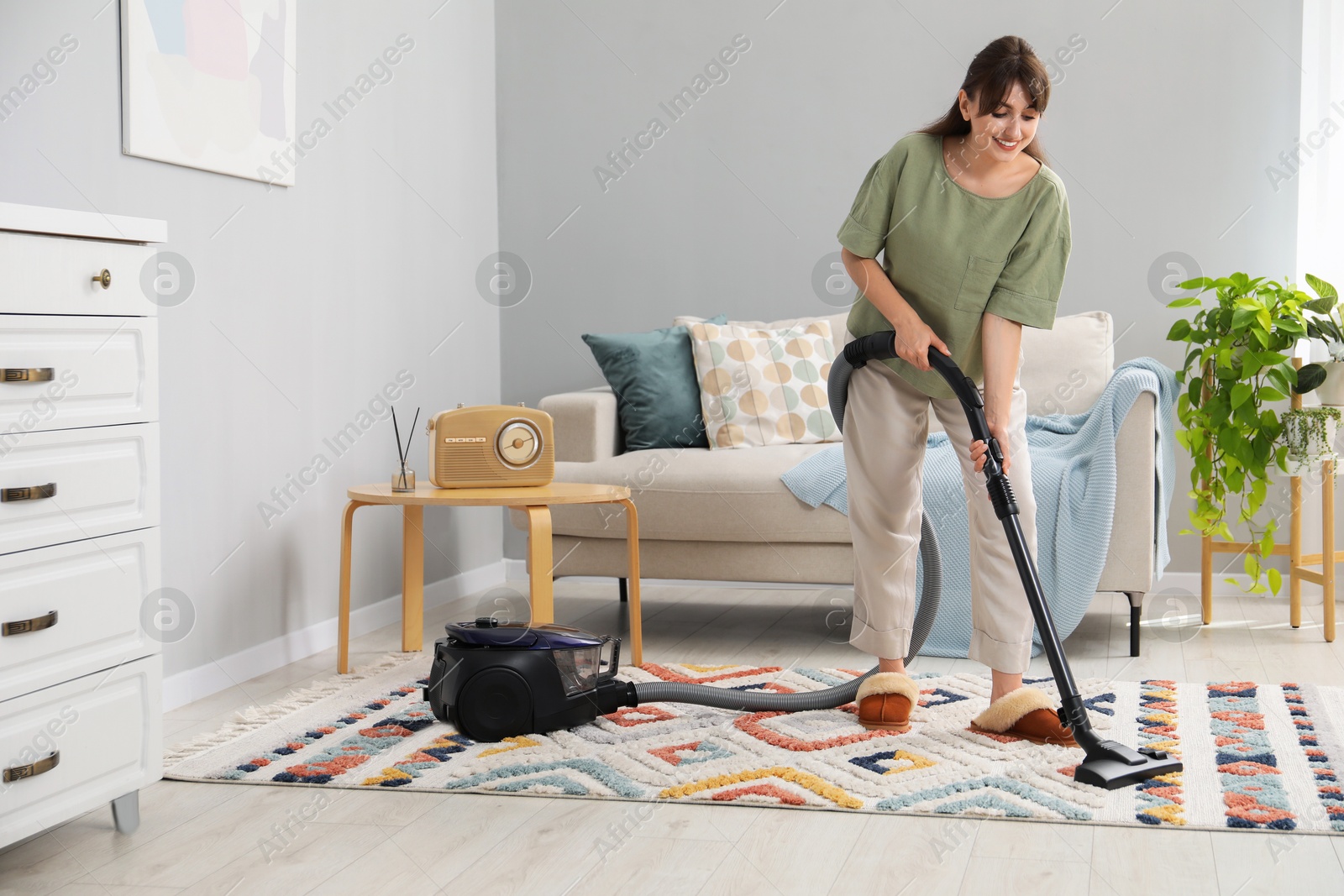 Photo of Young woman cleaning carpet with vacuum in living room