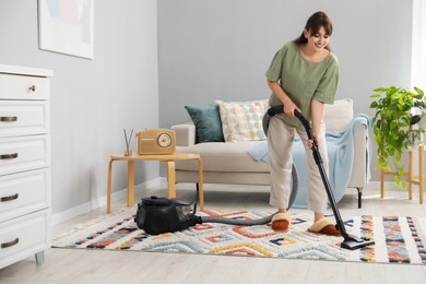 Young woman cleaning carpet with vacuum in living room