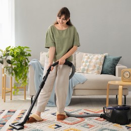 Young woman cleaning carpet with vacuum in living room