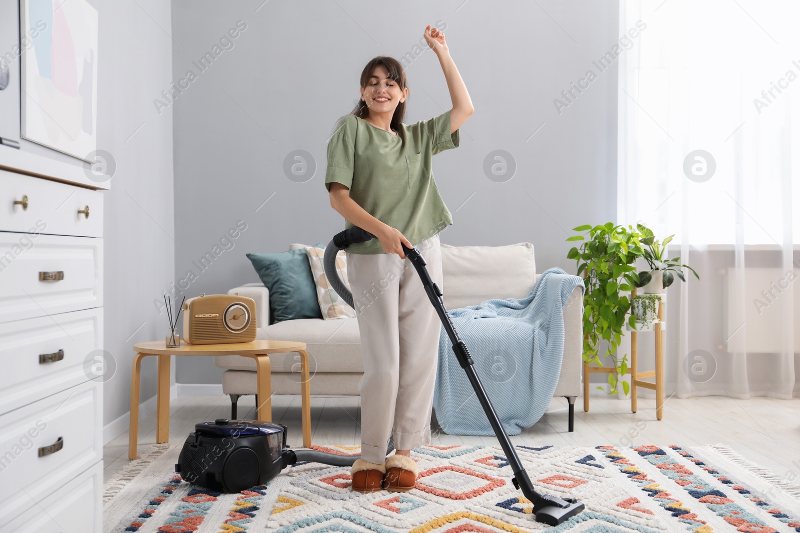 Photo of Young woman having fun while cleaning carpet with vacuum in living room