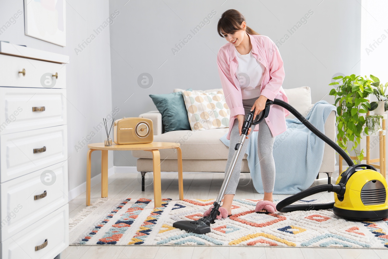 Photo of Young woman vacuuming carpet in living room