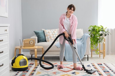 Photo of Young woman vacuuming carpet in living room