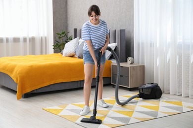 Photo of Young woman cleaning carpet with vacuum in bedroom