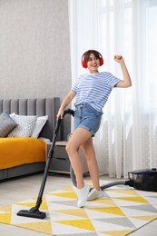 Young woman with headphones having fun while vacuuming carpet in bedroom