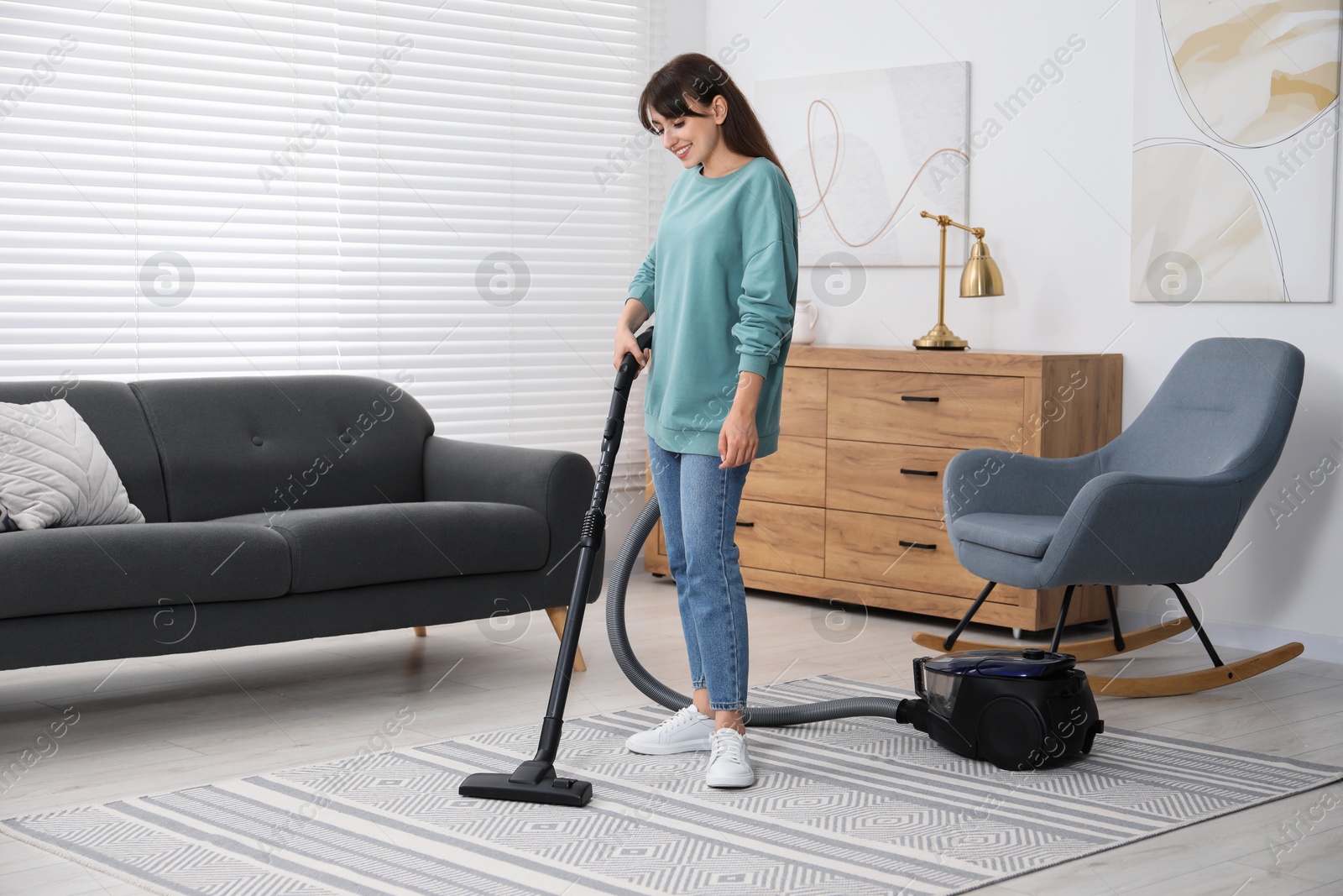 Photo of Young woman vacuuming carpet in living room