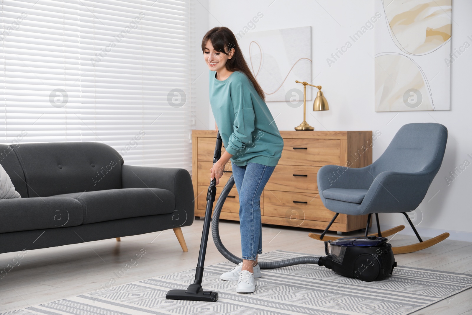 Photo of Young woman vacuuming carpet in living room