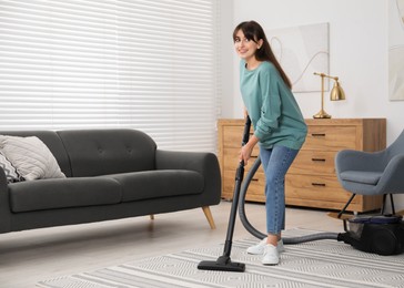 Photo of Young woman vacuuming carpet in living room