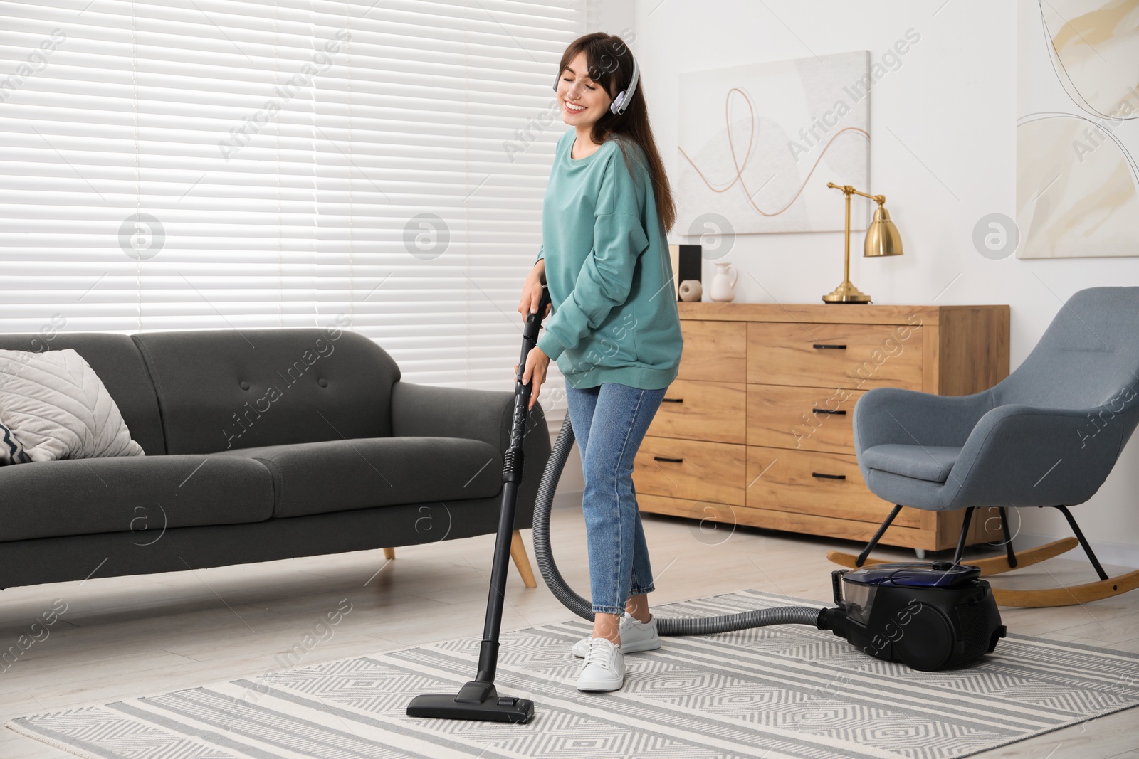 Photo of Young woman in headphones vacuuming carpet at home