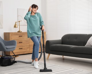 Young woman in headphones vacuuming carpet at home