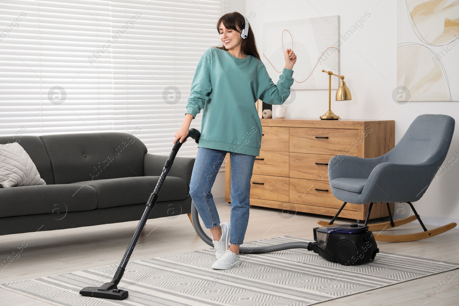 Photo of Young woman in headphones having fun while vacuuming carpet at home