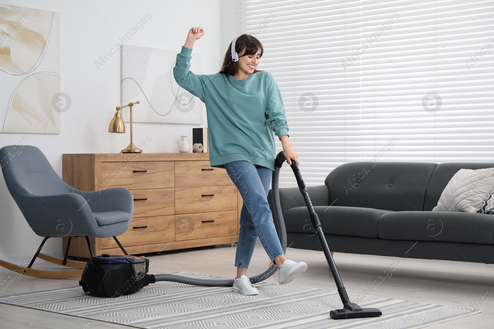 Photo of Young woman in headphones having fun while vacuuming carpet at home