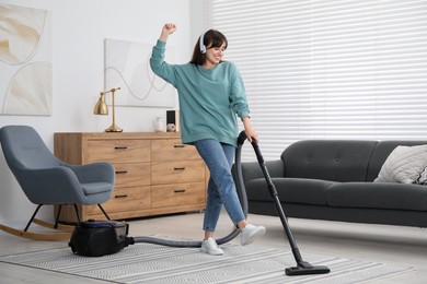 Young woman in headphones having fun while vacuuming carpet at home