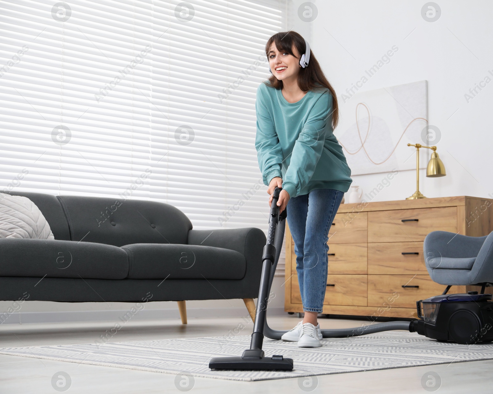 Photo of Young woman in headphones vacuuming carpet at home, low angle view