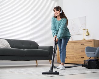 Young woman in headphones vacuuming carpet at home, low angle view