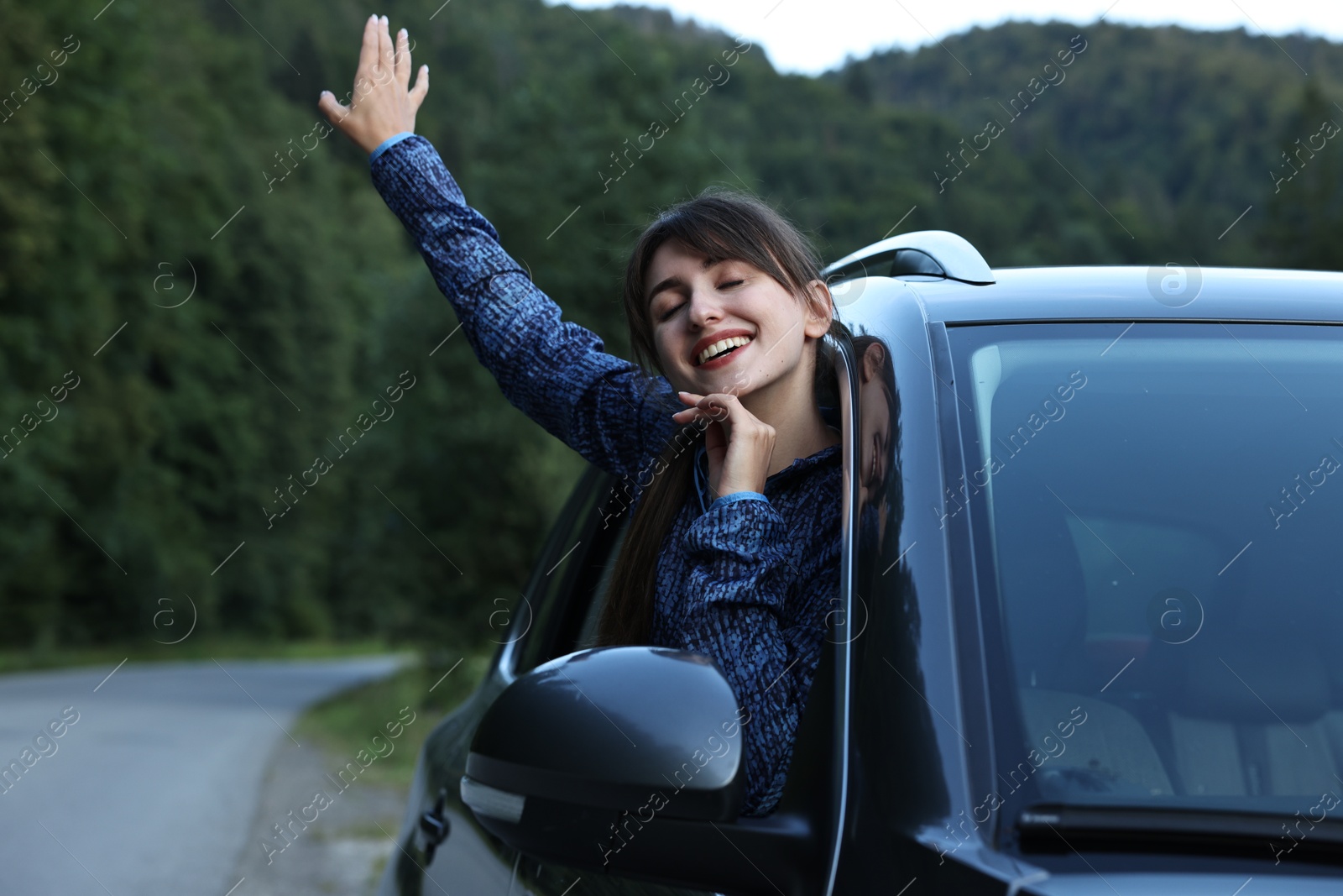 Photo of Smiling woman leaning out of car window in beautiful mountains