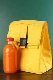 Photo of Lunch bag and bottle of juice on wooden table against color background