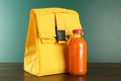 Photo of Lunch bag and bottle of juice on wooden table against color background