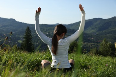 Photo of Woman on green grass in beautiful mountains, back view