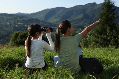 Women with binoculars on green grass in beautiful mountains, back view