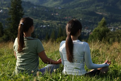 Women on green grass in beautiful mountains, back view