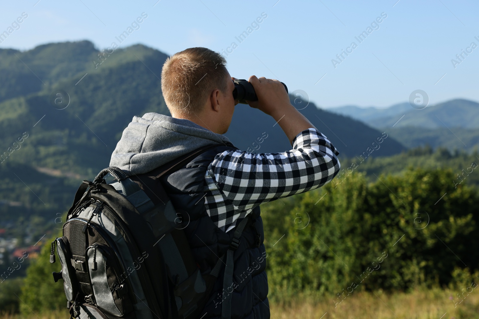 Photo of Man with backpack looking through binoculars in beautiful mountains, back view