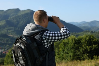 Photo of Man with backpack looking through binoculars in beautiful mountains, back view