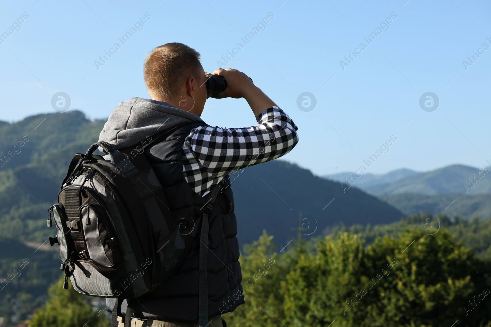 Photo of Man with backpack looking through binoculars in beautiful mountains, back view