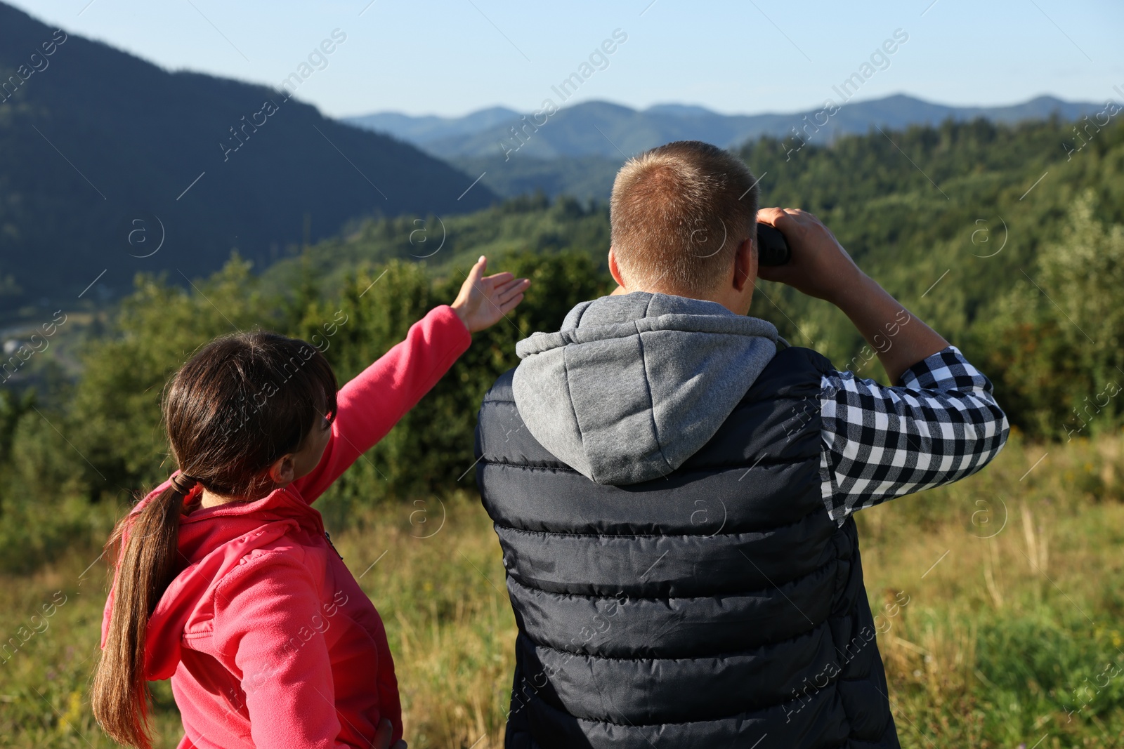 Photo of Couple with binoculars in beautiful mountains on sunny day, back view