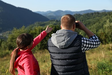 Couple with binoculars in beautiful mountains on sunny day, back view