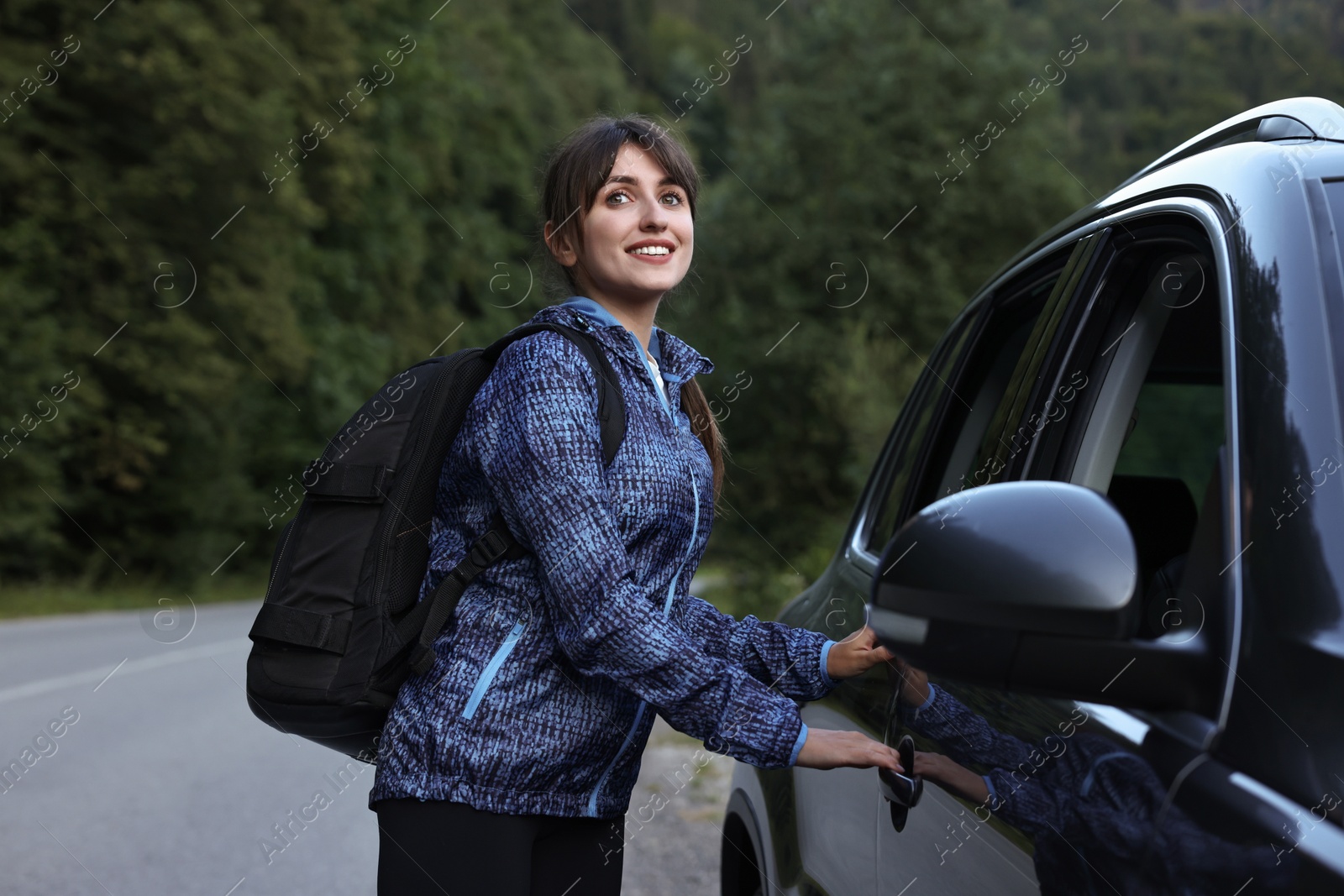 Photo of Smiling woman with backpack near car in beautiful mountains