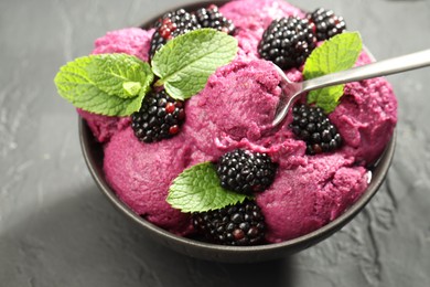 Photo of Taking delicious blackberry sorbet from bowl at gray textured table, closeup