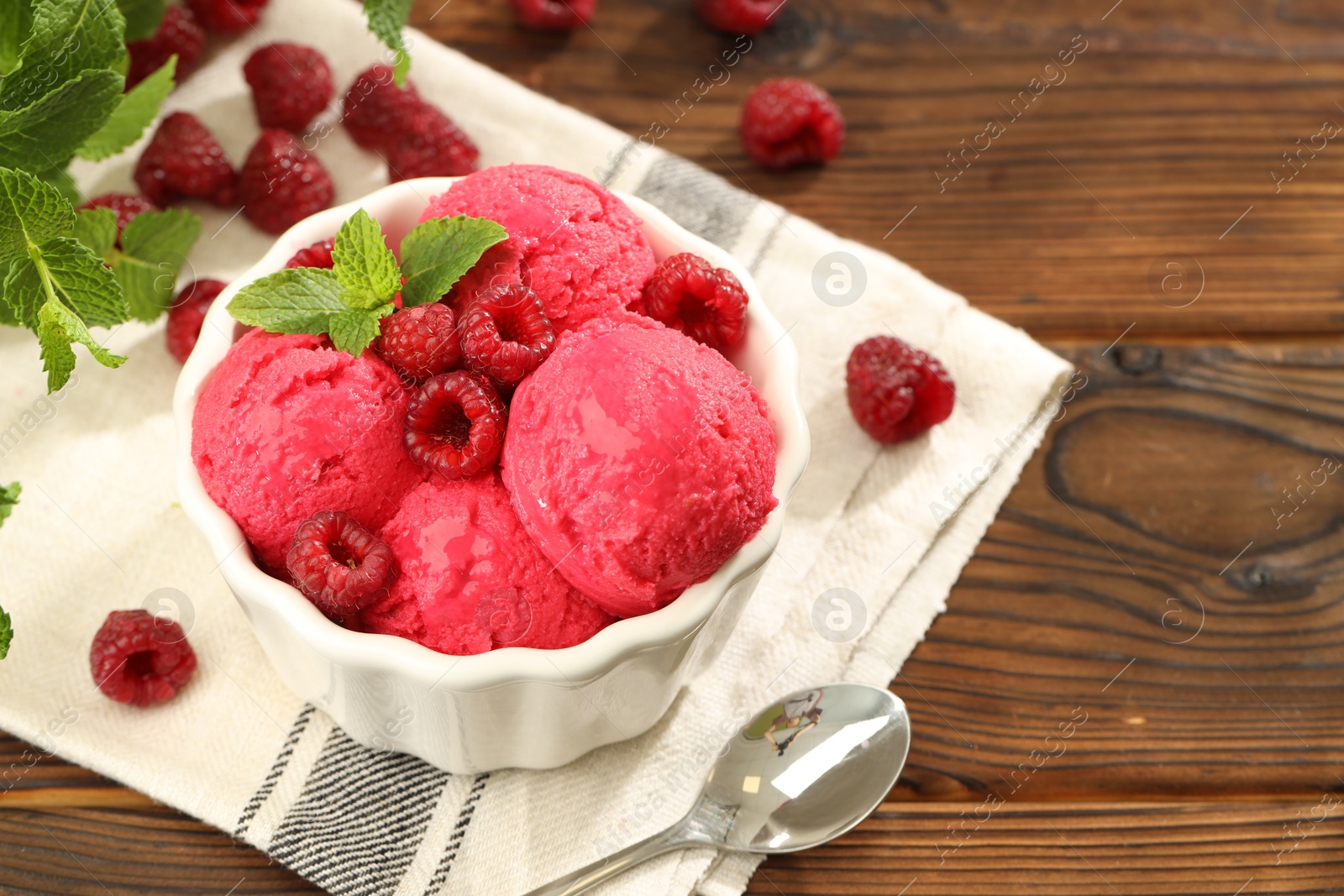 Photo of Delicious raspberry sorbet with fresh berries in bowl and spoon on wooden table, closeup