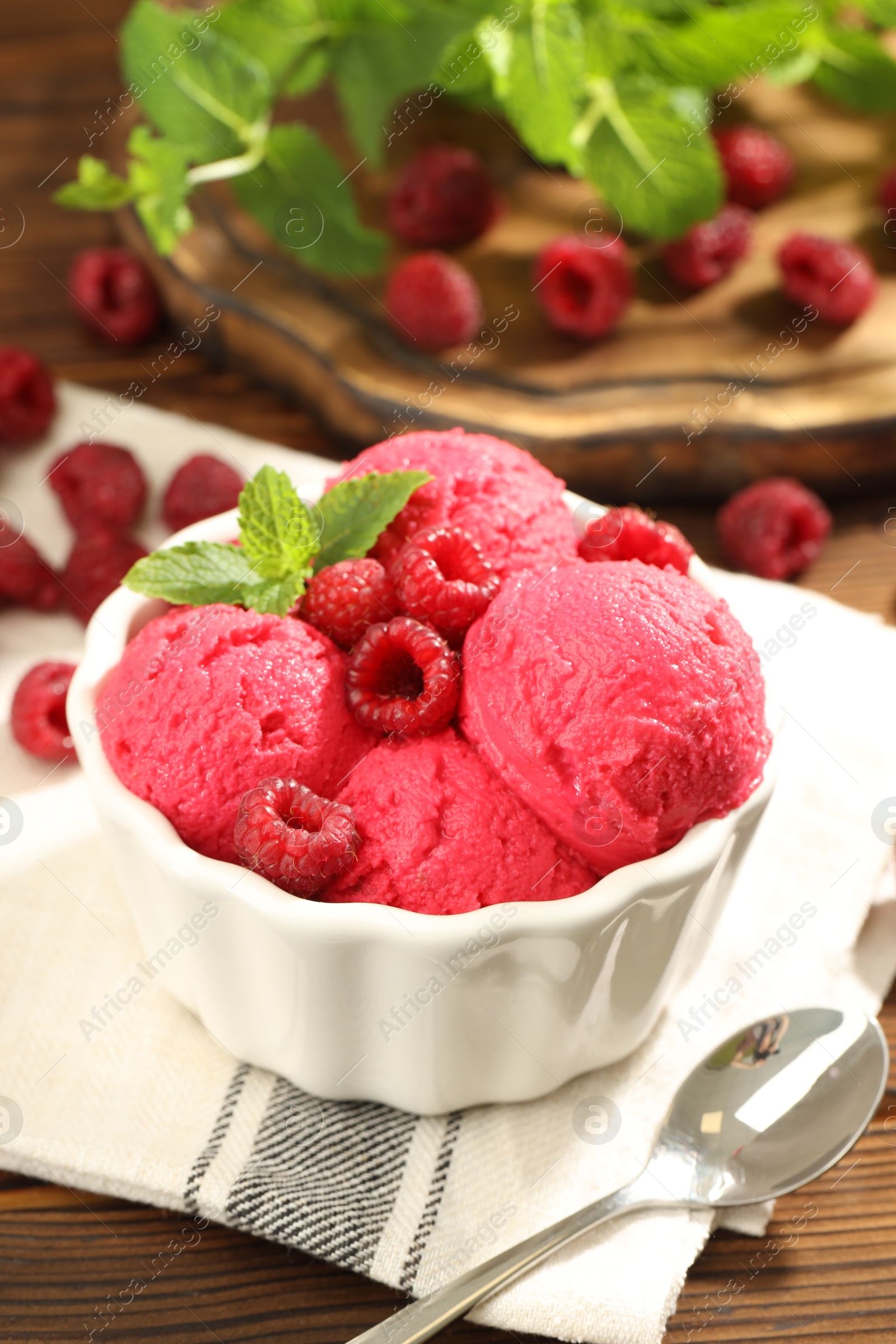 Photo of Delicious raspberry sorbet with fresh berries in bowl and spoon on wooden table