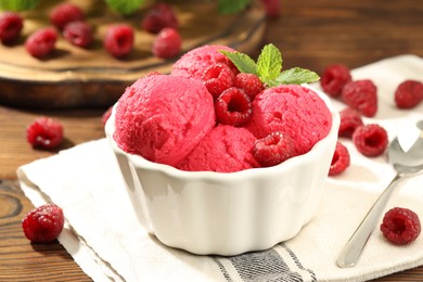 Photo of Delicious raspberry sorbet with fresh berries in bowl and spoon on wooden table, closeup