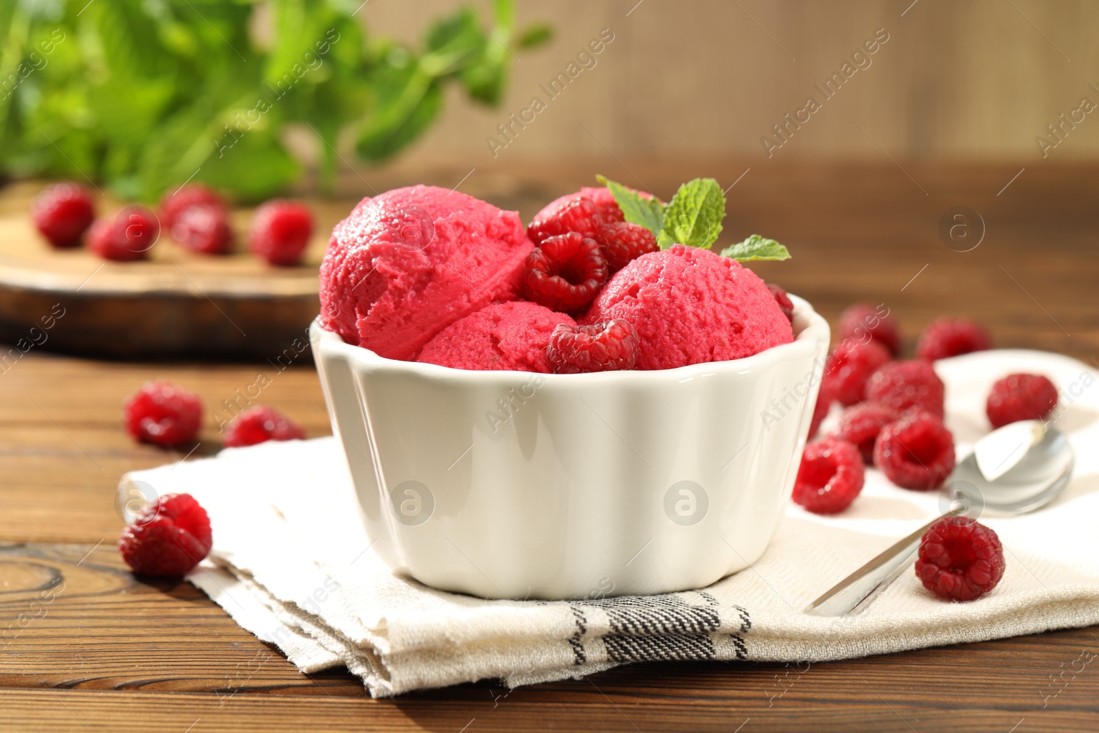 Photo of Delicious raspberry sorbet with fresh berries in bowl and spoon on wooden table, closeup