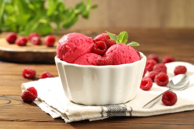 Photo of Delicious raspberry sorbet with fresh berries in bowl and spoon on wooden table, closeup