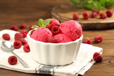 Photo of Delicious raspberry sorbet with fresh berries in bowl and spoon on wooden table, closeup