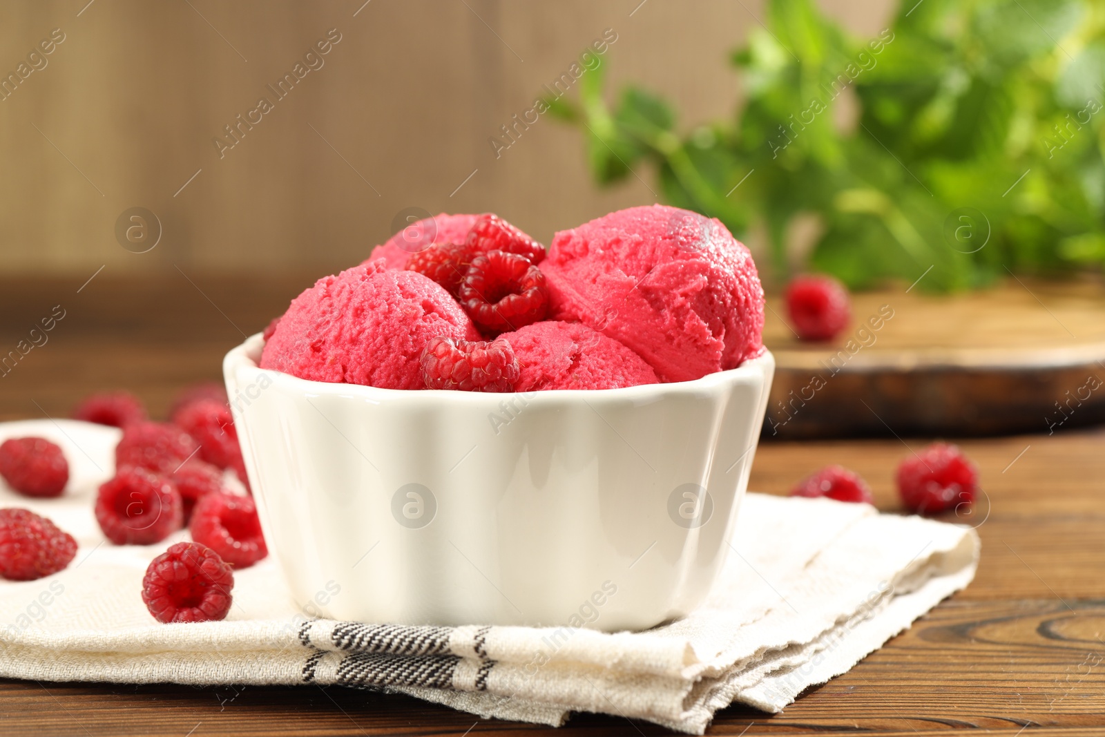 Photo of Delicious raspberry sorbet, fresh berries and mint in bowl on wooden table