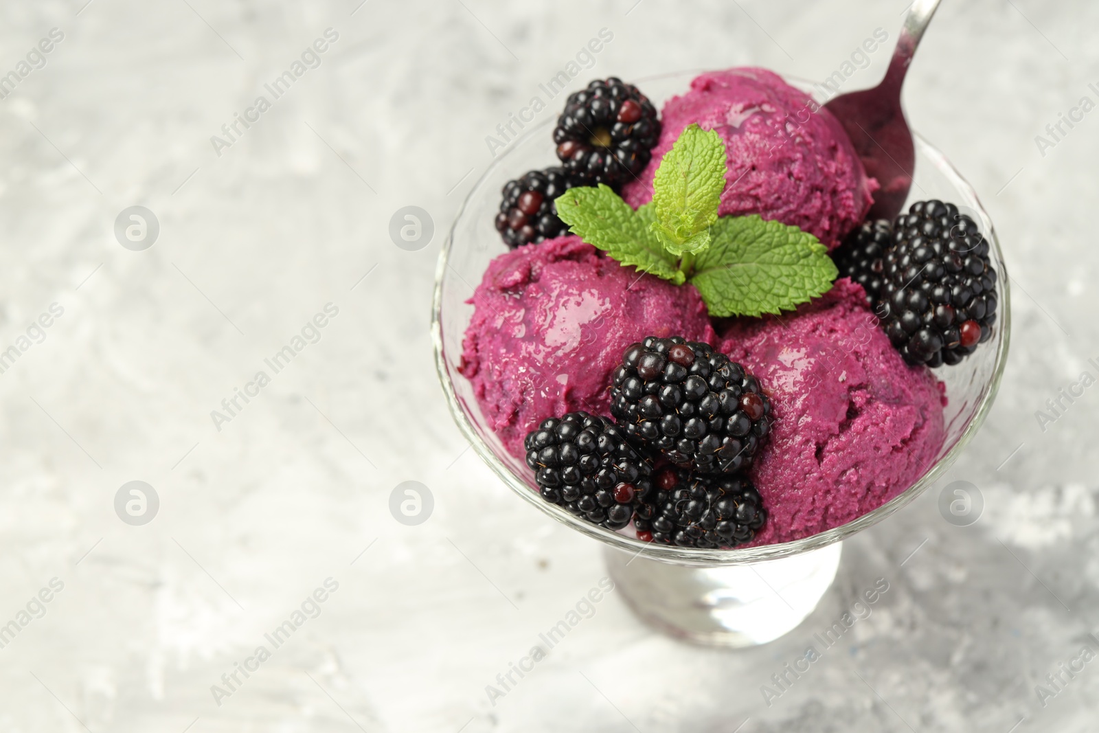 Photo of Delicious blackberry sorbet, fresh berries and mint in glass dessert bowl served on gray textured table, closeup. Space for text