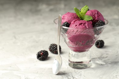 Photo of Delicious blackberry sorbet with fresh berries in bowl and spoon on gray textured table, space for text