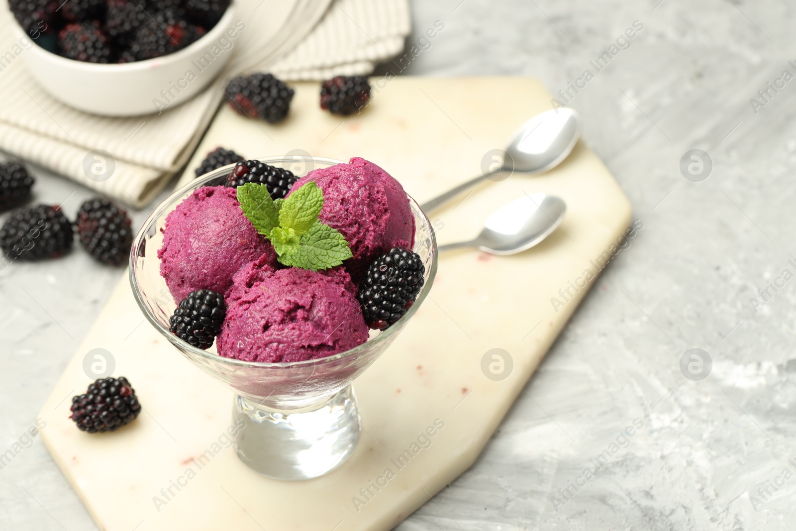 Photo of Delicious blackberry sorbet, fresh berries and mint in glass dessert bowl on gray textured table