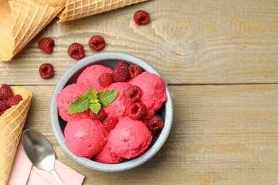 Photo of Delicious raspberry sorbet with fresh berries in bowl, waffle cones and spoon on wooden table, flat lay. Space for text