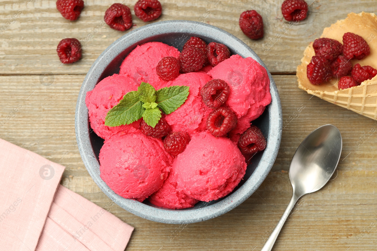 Photo of Delicious raspberry sorbet with fresh berries in bowl, waffle cone and spoon on wooden table, flat lay