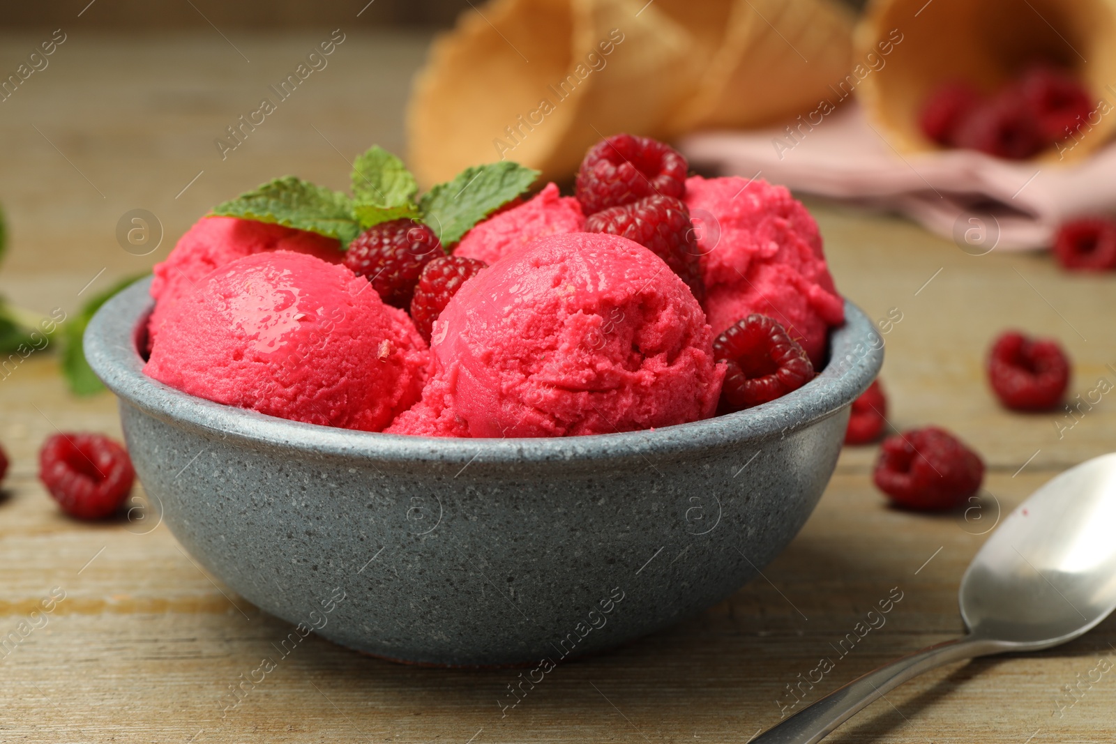 Photo of Delicious raspberry sorbet with fresh berries in bowl and spoon on wooden table, closeup