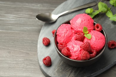 Photo of Delicious raspberry sorbet with fresh berries in bowl and spoon on wooden table, closeup