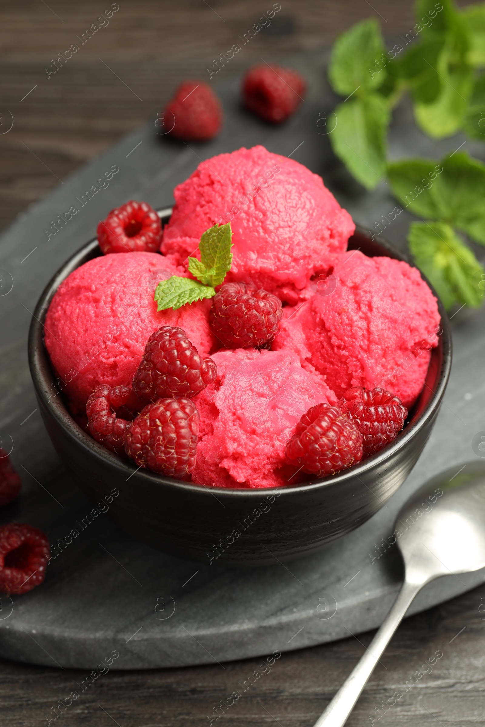 Photo of Delicious raspberry sorbet with fresh berries in bowl and spoon on wooden table, closeup