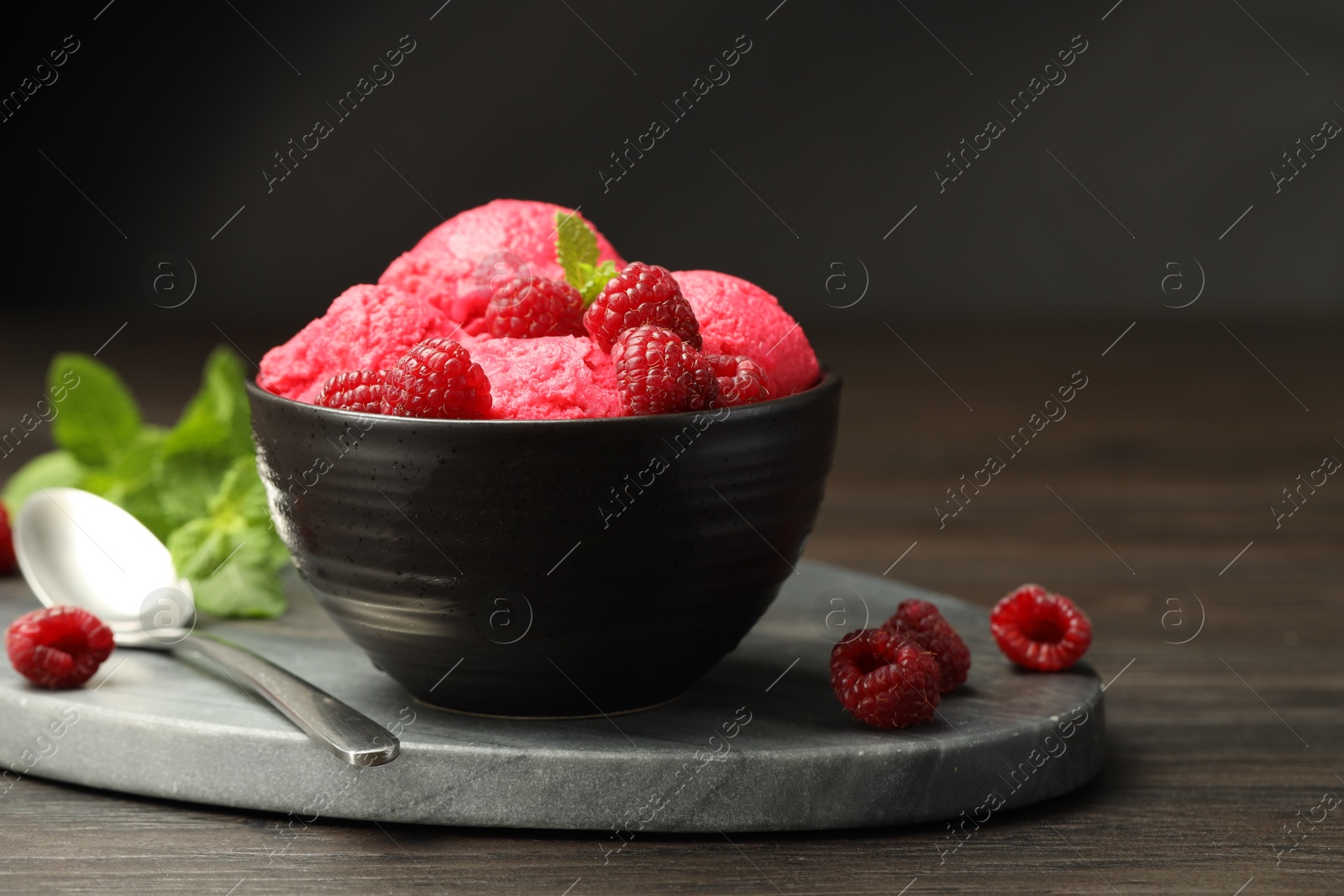 Photo of Delicious raspberry sorbet with fresh berries in bowl and spoon on wooden table