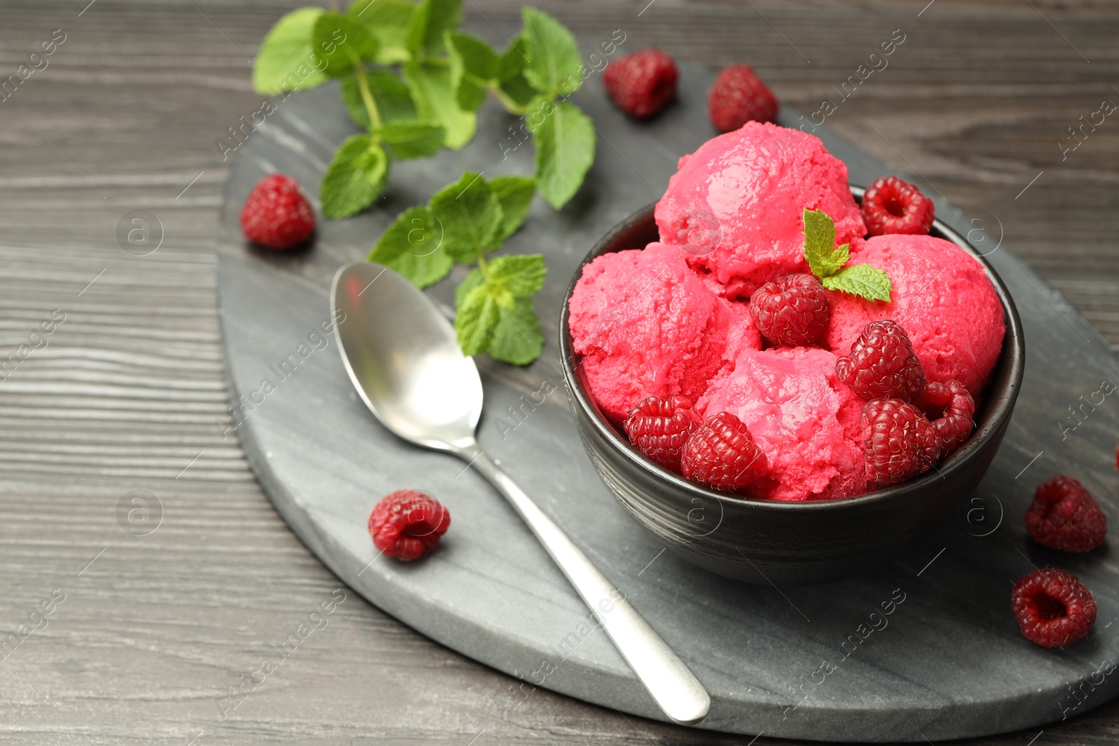 Photo of Delicious raspberry sorbet in bowl, fresh berries, mint and spoon on wooden table, closeup